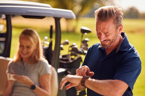 Man Checking Watch As Mature Couple Sit In Buggy And Play Round Of Golf Together